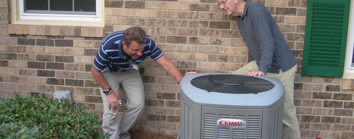 Two men look at an outdoor AC unit