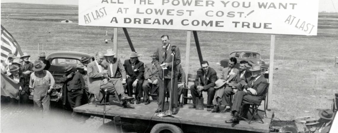A black and white photo of a group of men on a makeshift stage advertising power.