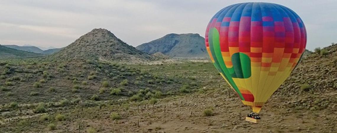 A rainbow-colored hot air balloon flies over the desert.