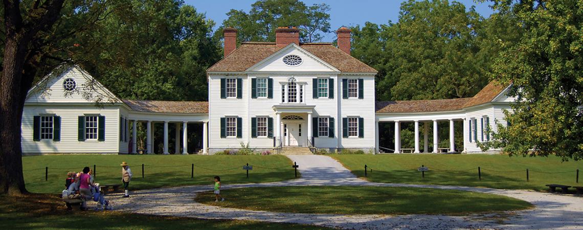 A large, sprawling white house is pictured surrounded by greenery.