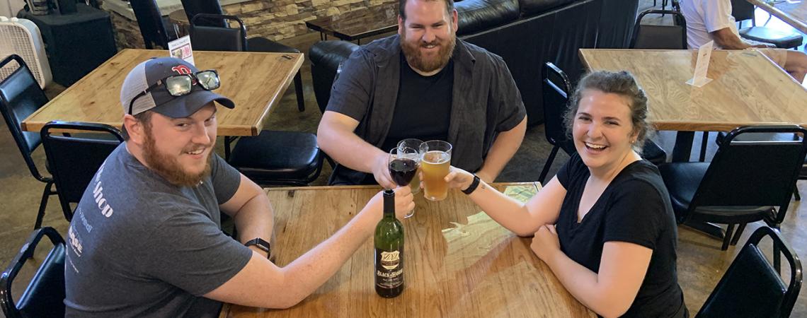 Three people smiling around a table enjoying drinks