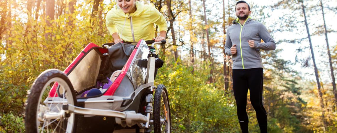 A couple jogs while pushing a child in a stroller