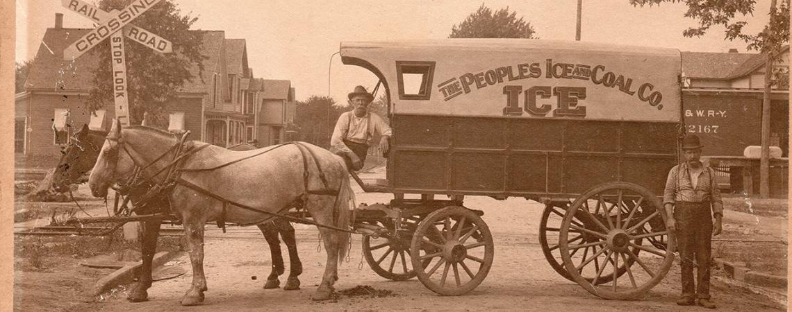 Two men pose with a wagon drawn by horses, designed to carry and deliver ice.