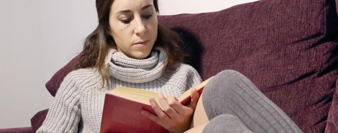 A woman reads a book on a couch.