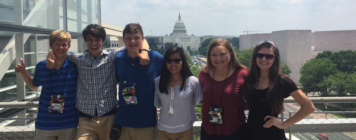 A group of kids smiles in front of the U.S. Capitol Building.