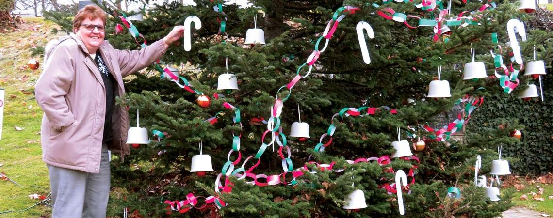 Martha Starkey hangs a decorative candy cane on the Christmas tree at the tomb of August Imgard.