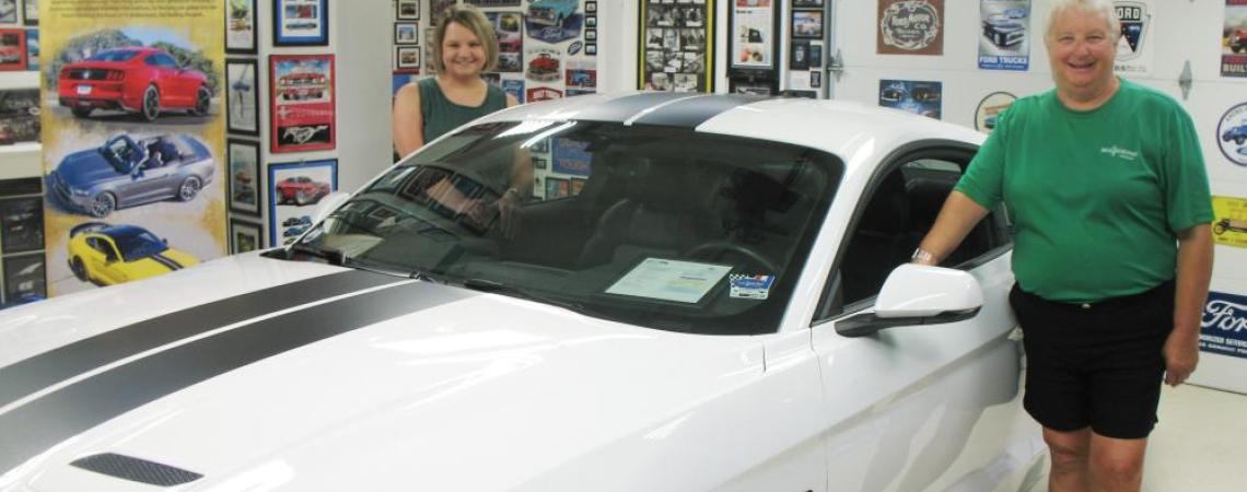 Two women posing with a mustang in a museum.