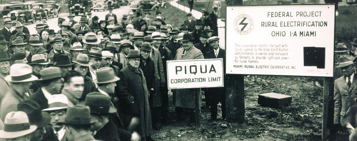 A black and white photo of Ohioans watching the setting of a utility pole