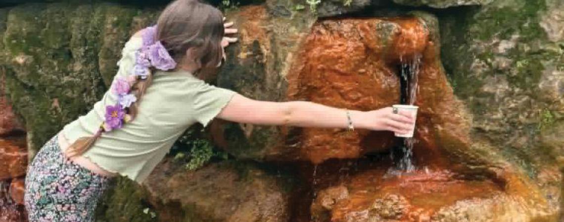 A girl holding a cup under a spring waterfall