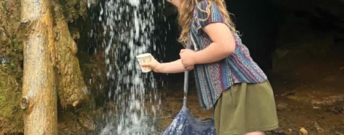 A girl holding a cup under a spring waterfall