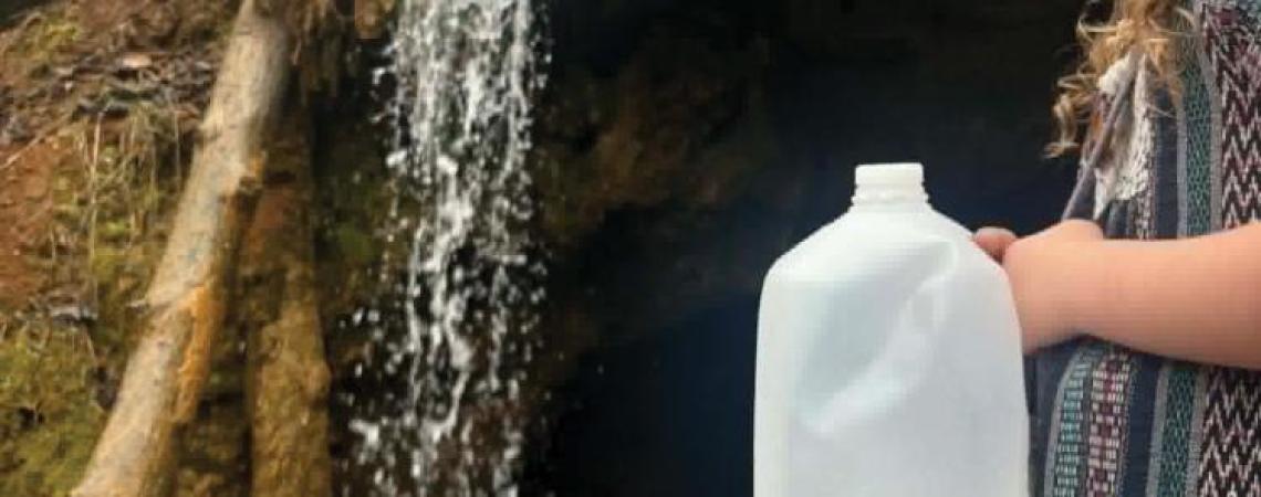 A girl holding a water jug beside a spring waterfall