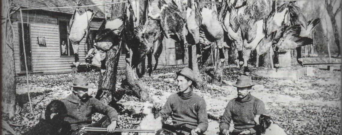 A black and white image of men sitting on the ground with guns after a duck hunt